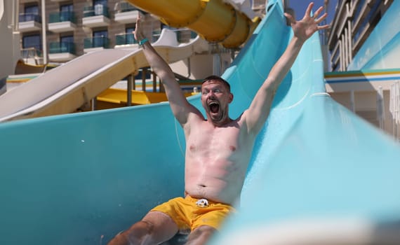 Joyful man slides down slide in water park