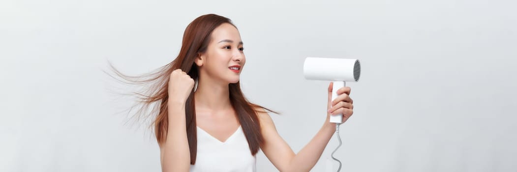 Woman dries her beautiful long hair with a hair dryer against a white background. Web banner