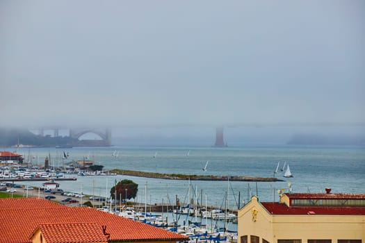 Foggy view of San Francisco Bay with boats and distant obscured Golden Gate Bridge