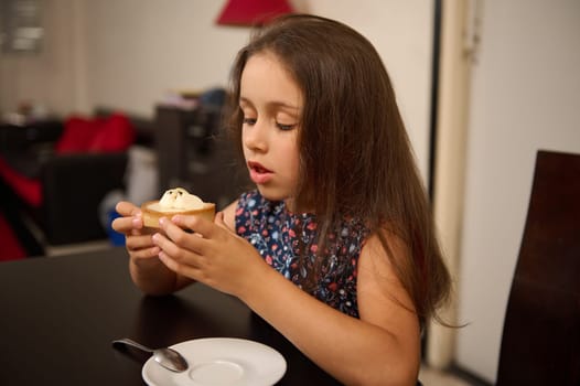 Beautiful Caucasian little girl in stylish casual dress, eating a delicious lemon cake at home. Sweet food concept