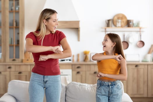 Positive attractive blonde millennial woman mother and cute girl teenager daughter having fun dancing at home, moving their arms bodies, looking at each other and smiling, enjoying time together