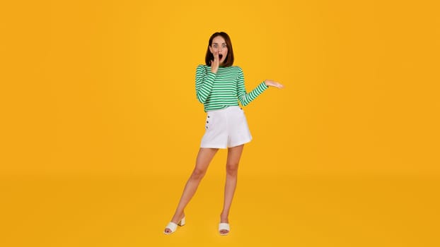 Amazed pretty young woman showing blank space on yellow background