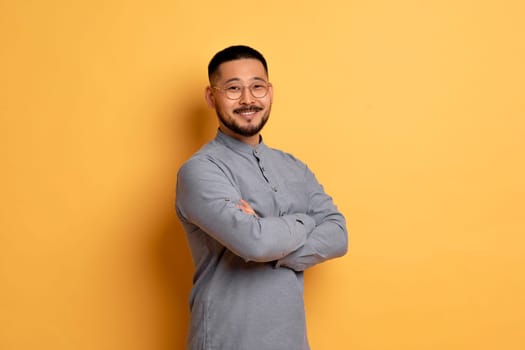 Portrait of confident asian man standing with folded arms on yellow background