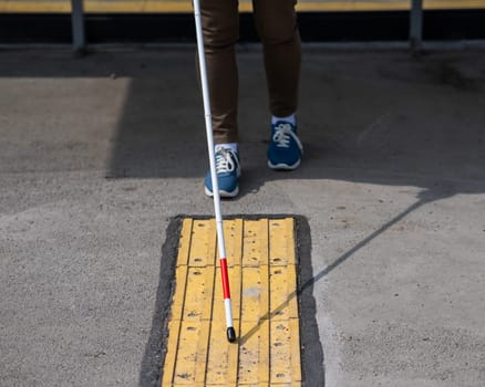 Close-up of the legs of a blind woman at a bus stop.