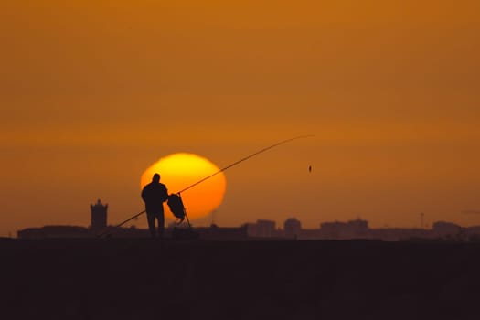 A man is fishing at sunset standing on the hill