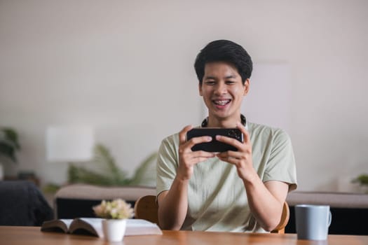 Happy man using mobile phone. Smiling young male using smartphone play social media relax on sofa at home.