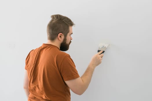 Man smoothes wall surface with a wall grinder. Male grind a white plaster wall - renovation and redecoration concept