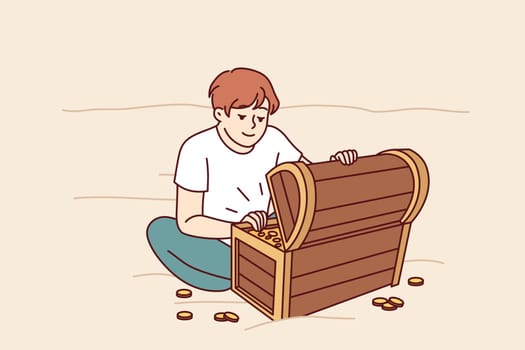 Treasure hunter boy found wooden chest with gold and is sitting on beach looking at prey