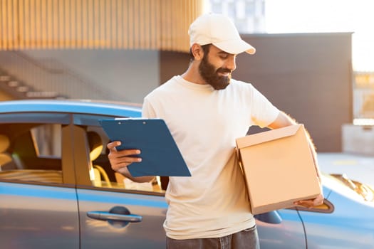 Indian courier standing near his car holds parcel box outdoors
