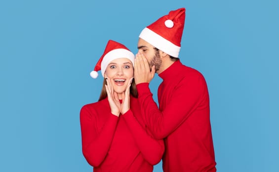 Young Man In Santa Hat Whispering Christmas Secret To His Excited Girlfriend
