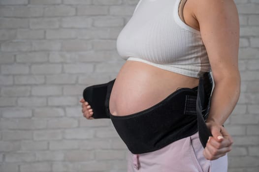 A pregnant woman puts on a black two-piece bandage. Cropped tummy.