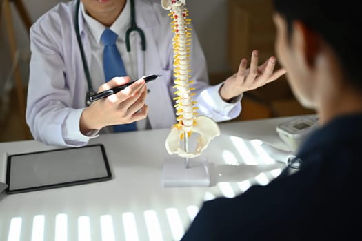 Experienced male orthopedist giving consultation about scoliosis or spinal problems during medical exam