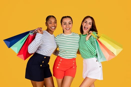 Cute multiracial ladies enjoying shopping together, yellow background