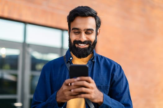 Portrait Of Smiling Bearded Arabian Man Using Smartphone Application Outdoor