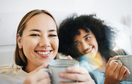 Coffee, smile and portrait of lesbian couple on bed in conversation for bond and relax together. Happy, rest and interracial lgbtq women laughing, talking and drinking latte in bedroom of apartment.
