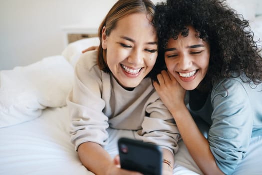 Cellphone, relax and young lesbian couple in bed networking on social media, mobile app or the internet. Happy, technology and interracial lgbtq women scroll on a phone in bedroom at modern apartment