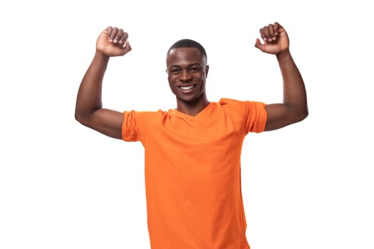 young american man in orange t-shirt with positivity raised his hands