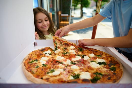 Smiling little girl looking at a cardboard box with Neapolitan traditional Italian Margherita pizza with a crispy crust