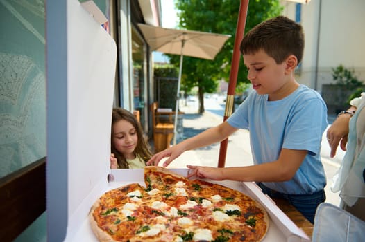Adorable children eating delicious freshly baked Italian Margherita pizza with crispy crust in the street