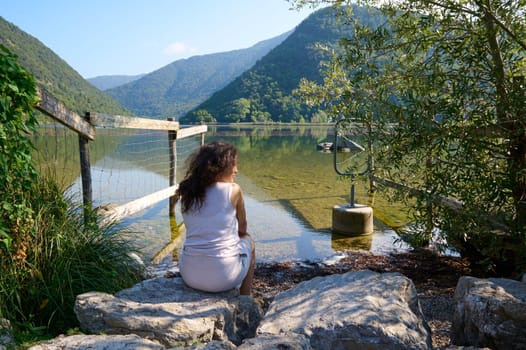 Rear view of a brunette woman sitting by a lake landscape. Discovering Italy. Segrino Lake in Italy, Lombardy. Travel and adventure.