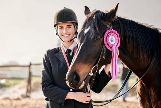 Portrait, equestrian and a woman winner with an animal on a ranch for sports, training or a leisure hobby. Smile, award or prize ribbon and a happy young rider in uniform with her stallion outdoor