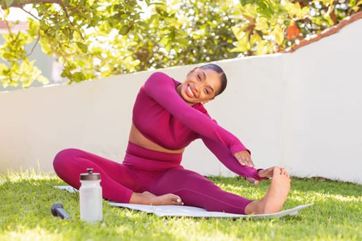 Athletic young black woman exercising on yoga mat at garden