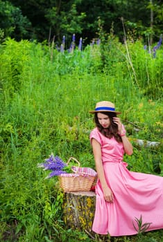beautiful girl in a beautiful dress sits on a stump in the forest, a bouquet of lupines in a basket.