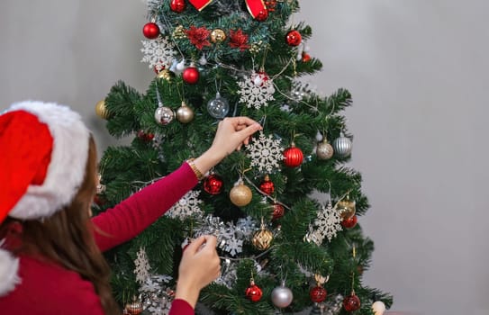Merry Christmas and Happy New Year Women is hands decorate the Christmas tree with balls and toys.
