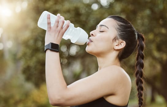 Woman, fitness and drinking water in nature for hydration, natural nutrition or sustainability. Thirsty runner person with mineral drink or bottle in rest after workout, exercise or outdoor training