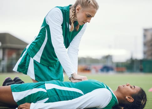First aid, cpr and accident with a hockey player on a field to save a player on her team during an emergency. Fitness, sports and heart attack with a woman helping her friend on a field of grass