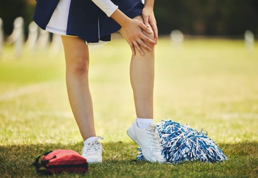 Cheerleader, injury and person with knee pain from sport, training and cheer exercise on a grass field. Health, accident and leg muscle bruise outdoor with emergency or workout challenge for wellness
