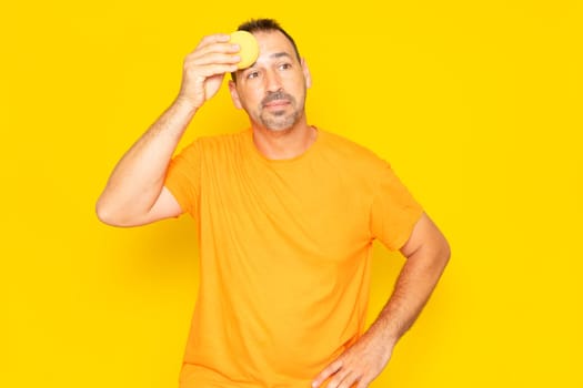 Hispanic man with beard in his 40s complaining about summer heat isolated on yellow background. Angry man wiping sweat with a sponge in hot weather. Stress, sweating, heat problem in summer.