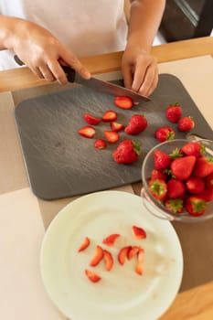 a woman slices strawberries with a knife in the kitchen
