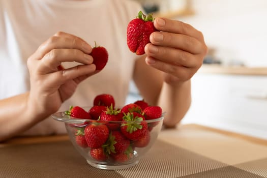 a woman's hands pulling strawberries out of a bowl