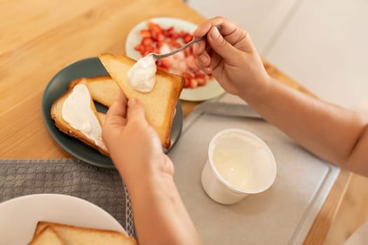 top view, a woman spreads sour cream on toast and puts strawberries on it
