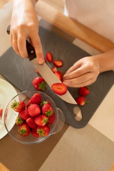 women's hands slicing strawberries on a board with a knife