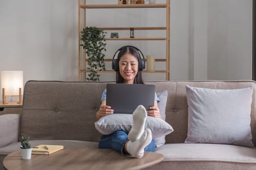 Woman listening music in headphones while lying on sofa in room