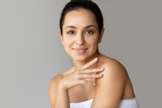 Woman posing touching smooth skin on shoulder over gray background