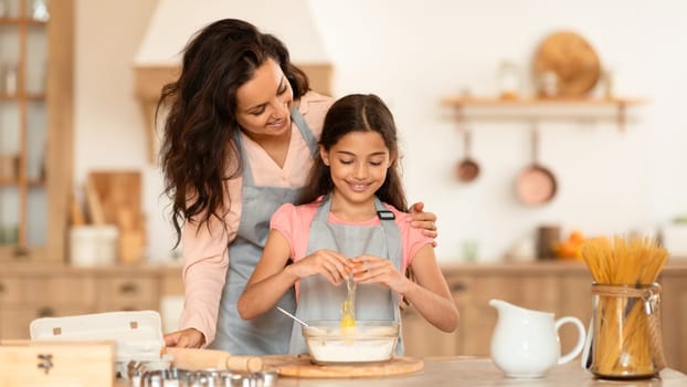 Mother And Daughter Adding Egg To Dough Preparing Cookies Indoor