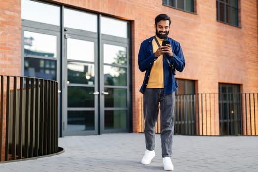 Full Length Of Indian Guy Using Application On Smartphone Outdoor