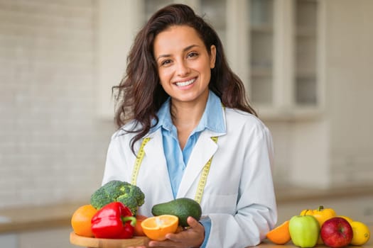 Portrait of smiling female nutritionist with plate of fresh fruits, working at weight loss clinic, smiling at camera