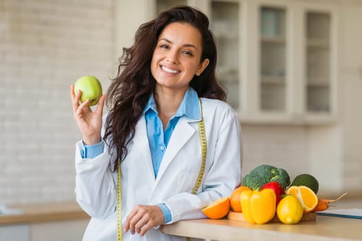 Cheerful female nutrition adviser with green apple and tape measure smiling at camera, promoting healthy eating habits