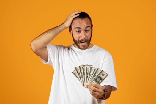Surprised happy adult european man in white t-shirt look at a lot of money dollars, do not believe to win