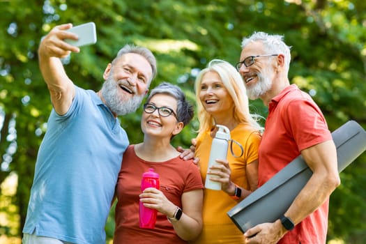 Group Of Sporty Senior People Taking Selfie Photo After Training Outdoors, Happy Older Men And Women In Activewear Holding Fitness Yoga Mats And Looking At Smartphone Camera, Enjoying Retirement