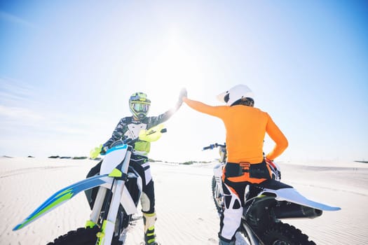 Extreme sport, motorcycle and desert with high five for achievement, skill and teamwork with success. Biker, sunshine and sand with adrenaline, fitness and congratulations for speed with training