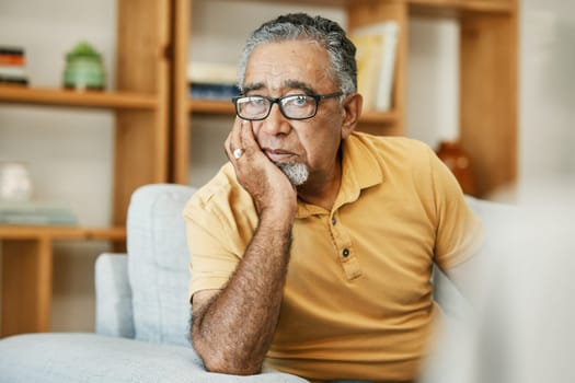 Face, mental health and thinking with a sad old man on a sofa in the living room of his retirement home. Depression, alzheimer or dementia and a senior person looking lonely with memory nostalgia