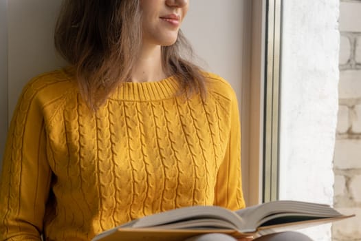 Young beautiful woman near window yellow knitted sweater read book