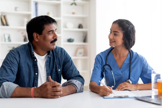 Smiling Indian Doctor Woman Talking To Male Patient During Appointment In Office