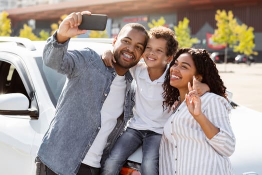 Happy beautiful young african american family taking selfie on cell phone with brand new auto. Black father, mother and preteen child son buying new car, capture exciting moment on phone