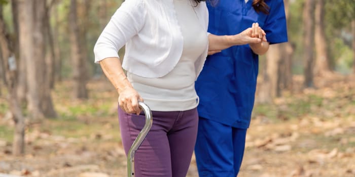 Nurse and senior in elderly care, support or walking with stick at park. Medical caregiver or therapist help patient or person with a disability in retirement or physiotherapy